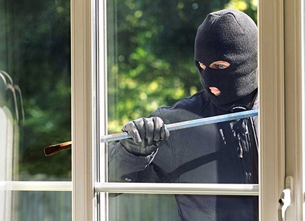 A burglar attempts to open a window with a crowbar.