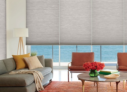 Honeycomb shades, window covering options, block an ocean view from a living room with red and grey furniture.