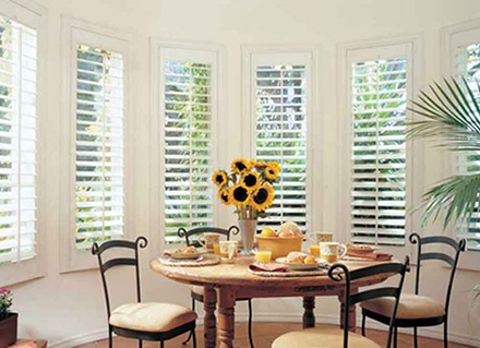 A dining nook has plantation shutters behind a small dining table in a home.