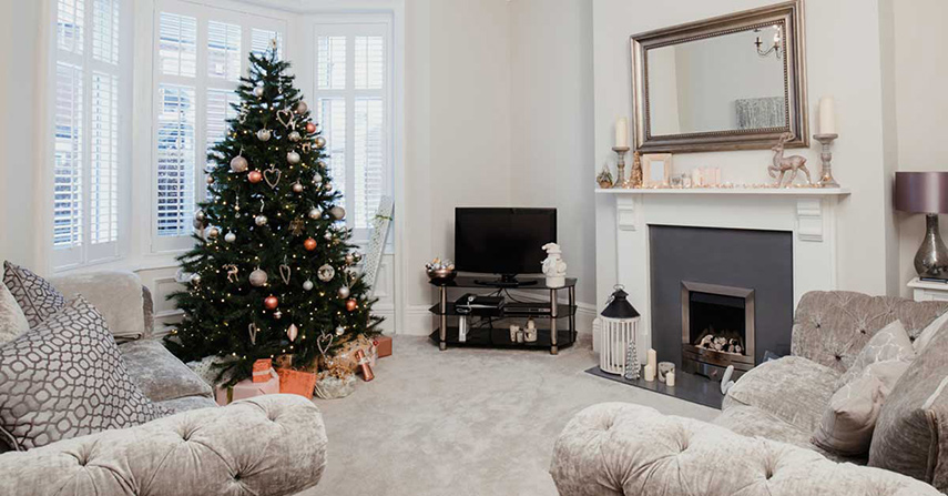 A holiday decorated living room with tree next to a window with tint and treatments.