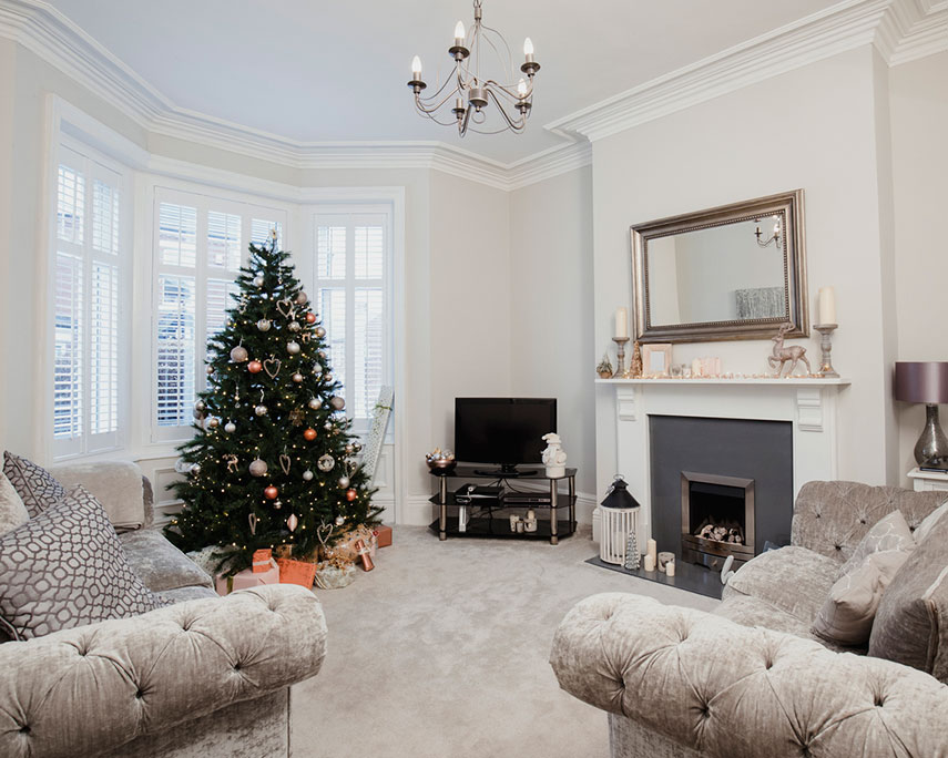A holiday decorated living room with tree next to a window with tint and treatments.