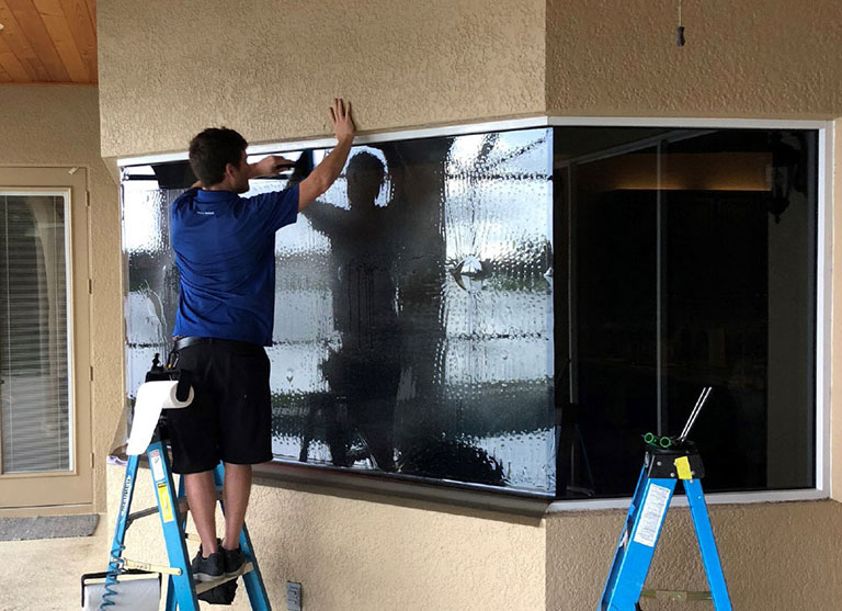 Man on stepladder installing window film on storefront
