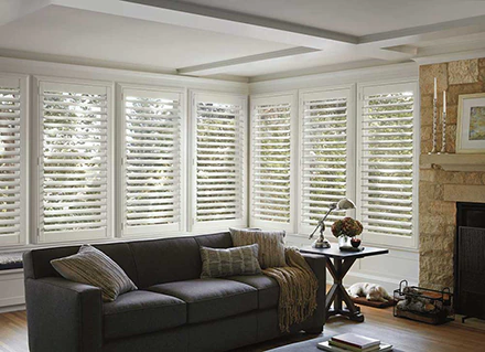 White colored NewStyle Lake Nona Plantation Shutters cover large bay windows of a modern living room.