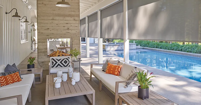 Exterior solar shades, another window treatment idea, are installed along a patio to protect the pool patio area from weather and heat.