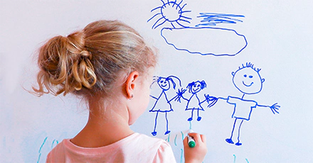 A child draws a stick figure family on a whiteboard.